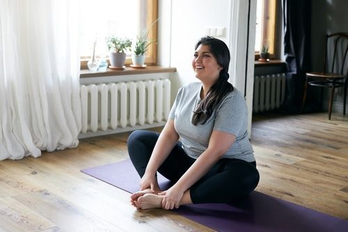 A woman is sitting on a yoga mat in a living room.