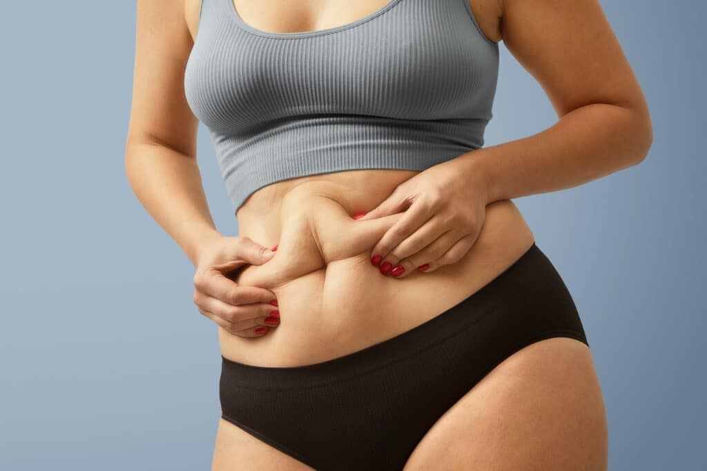 A woman in a crop top and black underwear is holding her belly.