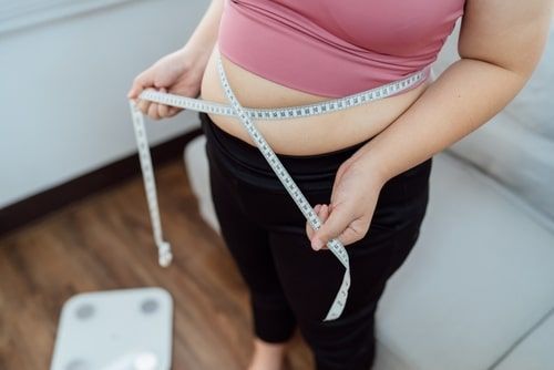 A woman is measuring her waist with a tape measure.