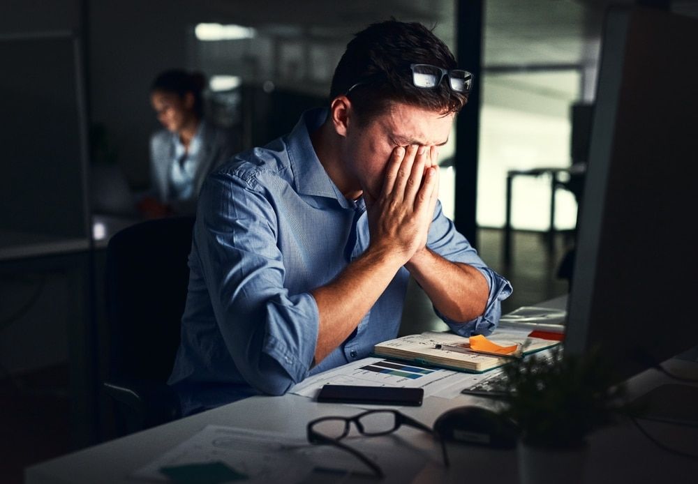 A man is sitting at a desk with his head in his hands.