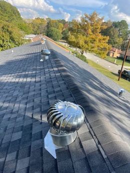 Roof with several shiny metal turbine vents, asphalt shingles, and a view of trees and a street.
