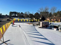 Construction site with a white roof, yellow safety flags, and a clear blue sky.