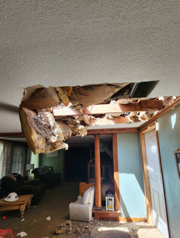 Collapsed ceiling in a home, debris scattered. Sunlight streams in. Interior view.