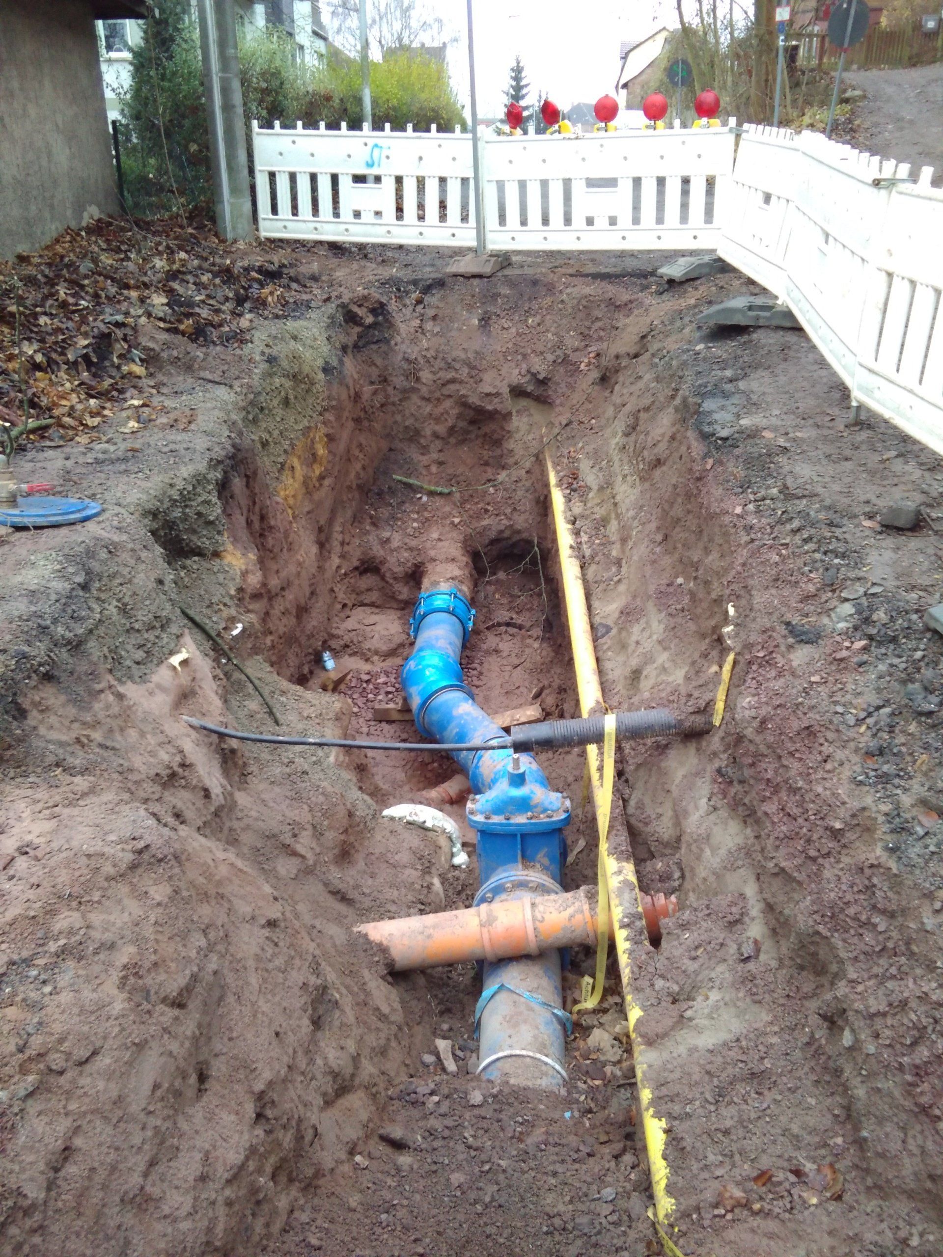 In einem Loch im Boden wird ein blaues Rohr verlegt.