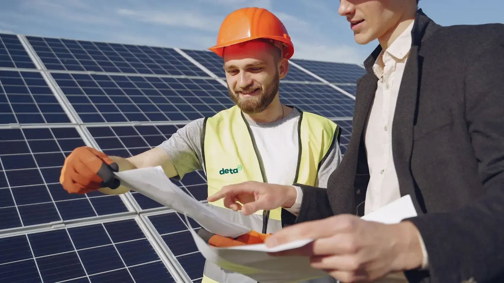 Two men are looking at a blueprint in front of a solar panel.