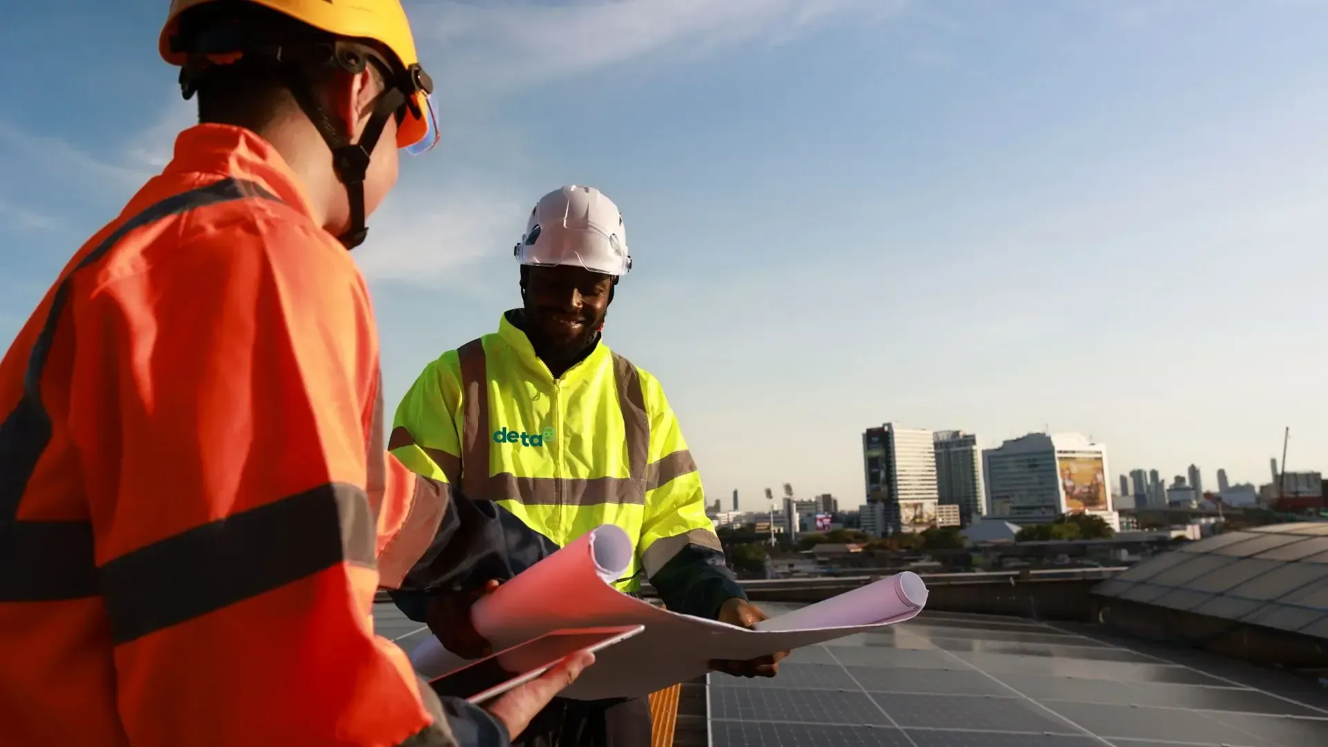 Two construction workers are looking at a blueprint on a rooftop.