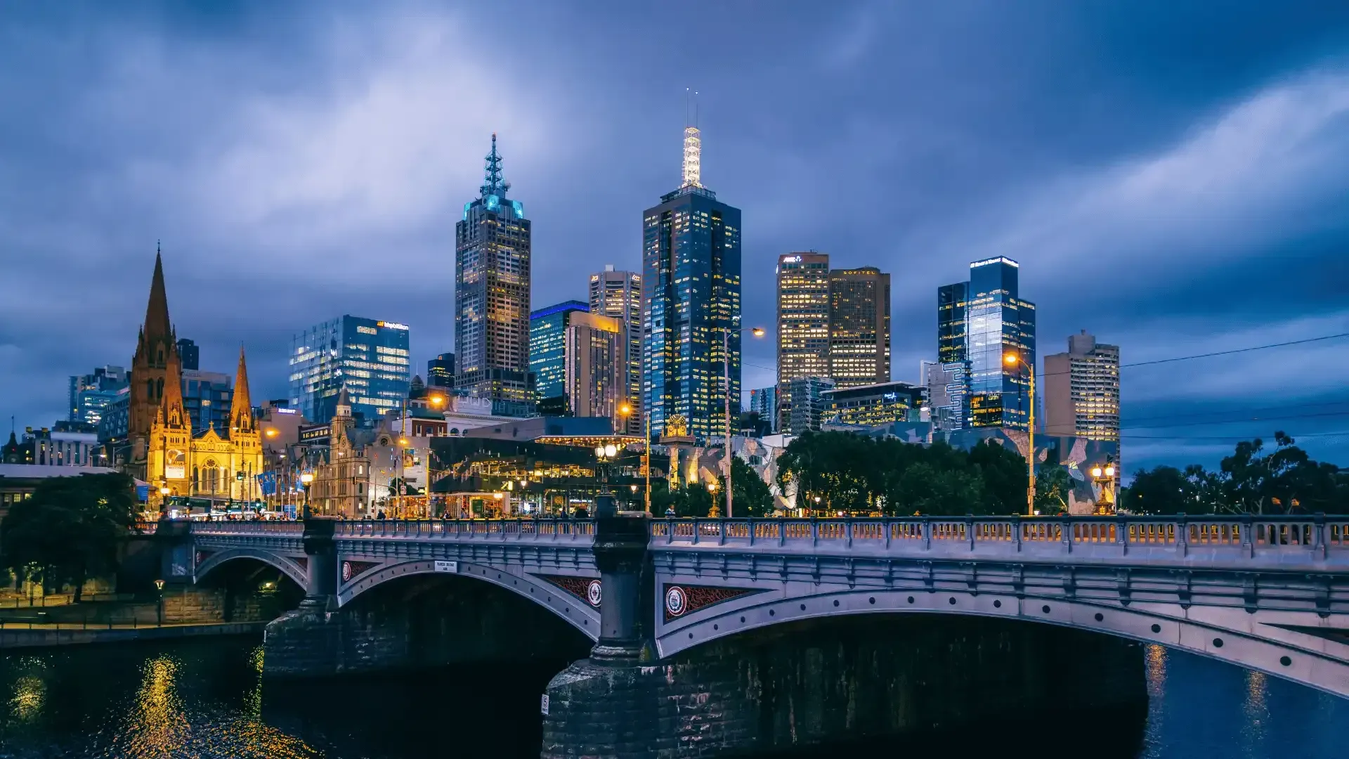A bridge over a river in front of a city skyline at night.
