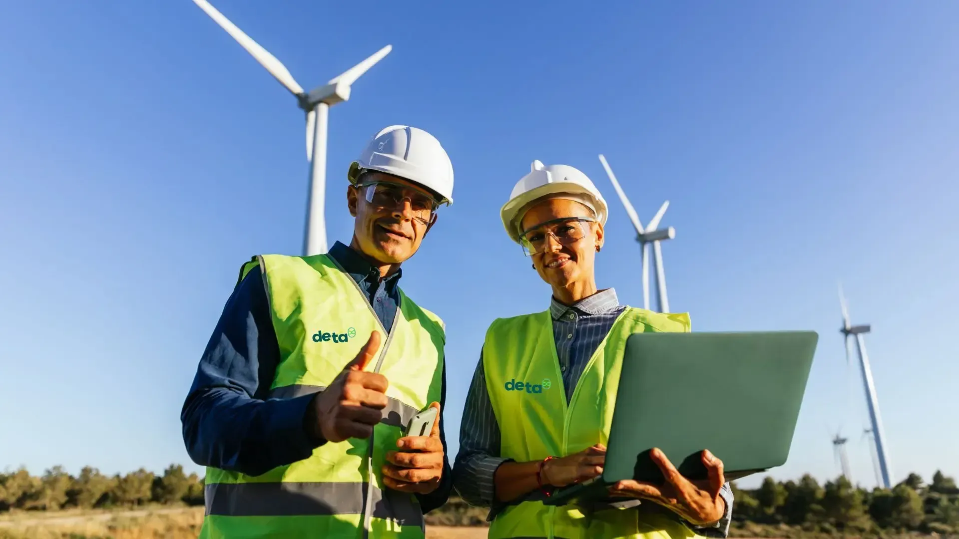 A man and a woman are standing next to each other in front of wind turbines.