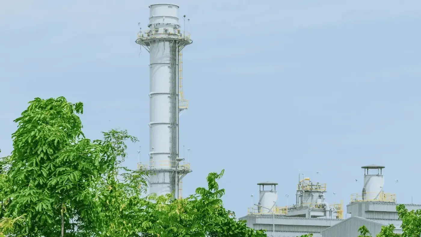 A large white chimney is surrounded by trees in a factory.
