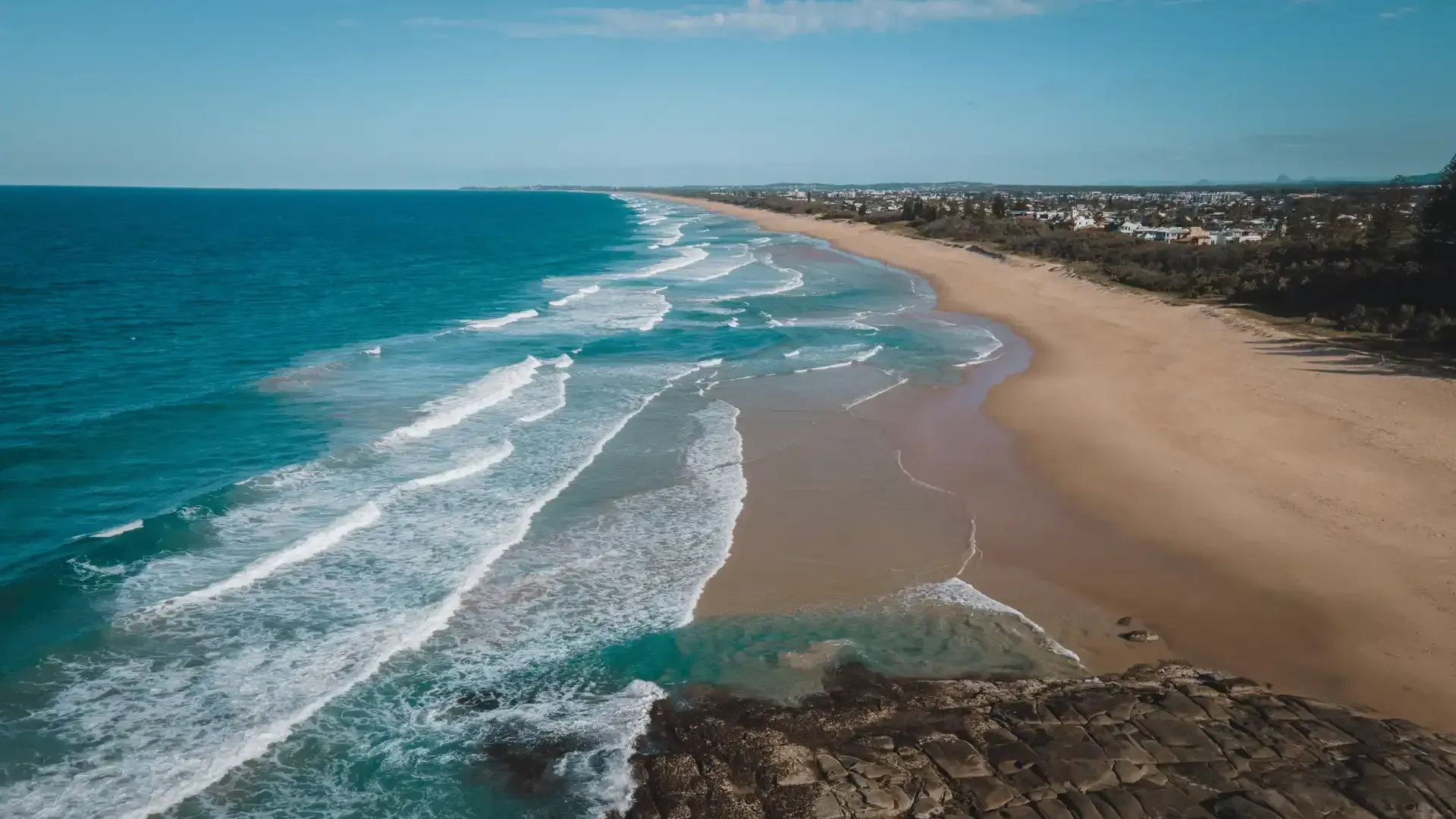 An aerial view of a beach with waves crashing on the shore.