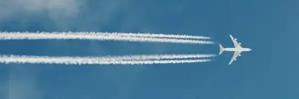 A plane is flying through a blue sky with smoke trails behind it.