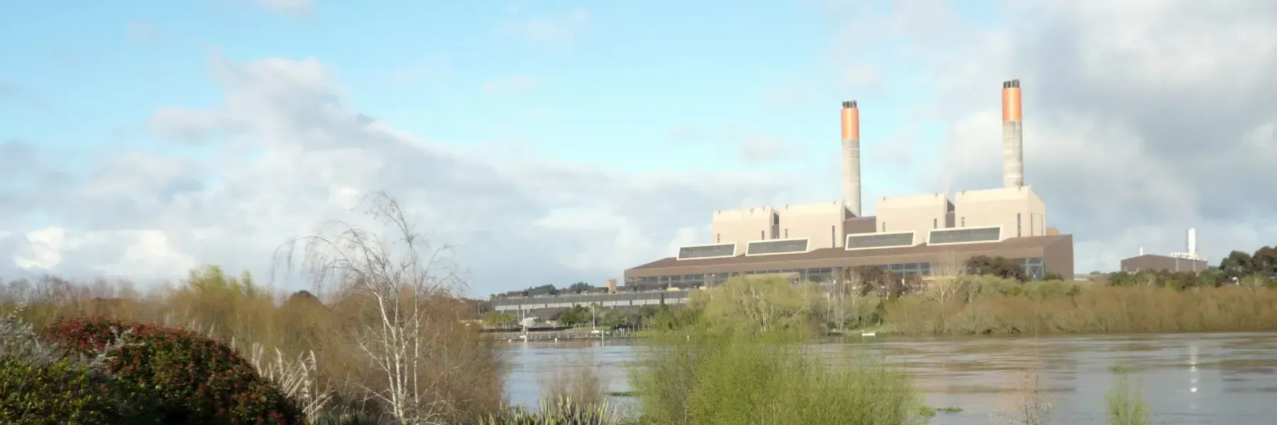 A large power plant is sitting next to a body of water.