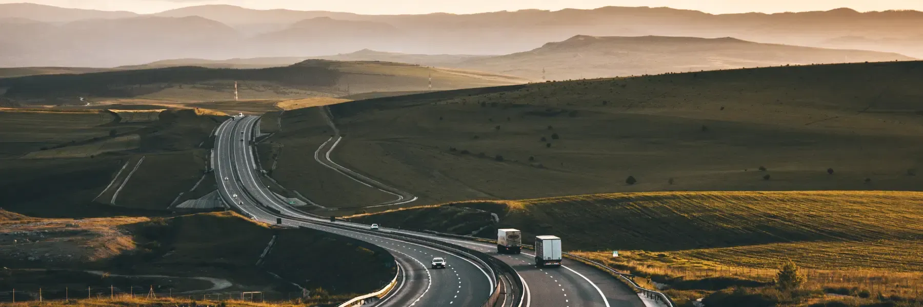 A highway winds through green hills at sunset.