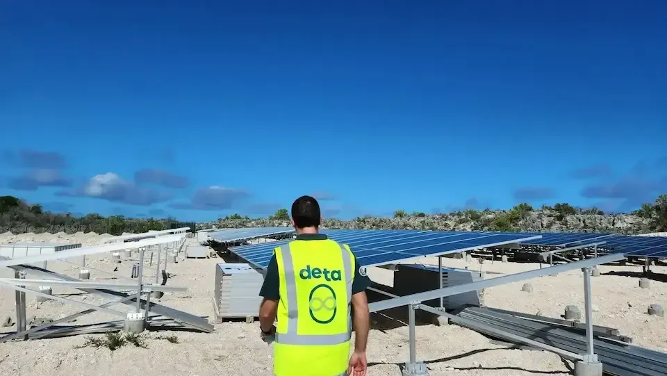 A man in a yellow vest is standing in front of a field of solar panels.