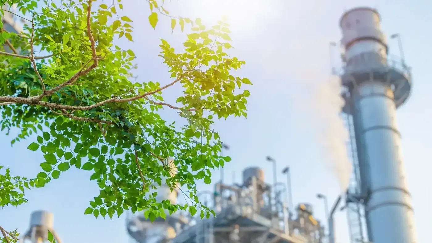 A factory with a tree in the foreground and a chimney in the background.