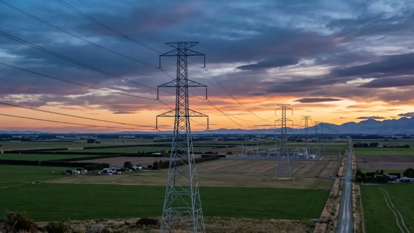 Transmission towers and power lines over green fields at sunset with a dramatic cloudy sky
