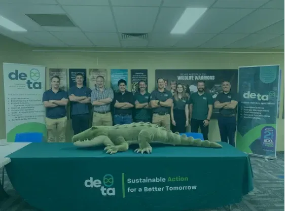 A group of people standing around a table with a stuffed alligator on it.