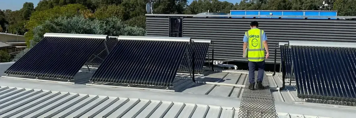 A man in a yellow vest is standing on top of a roof with solar panels.