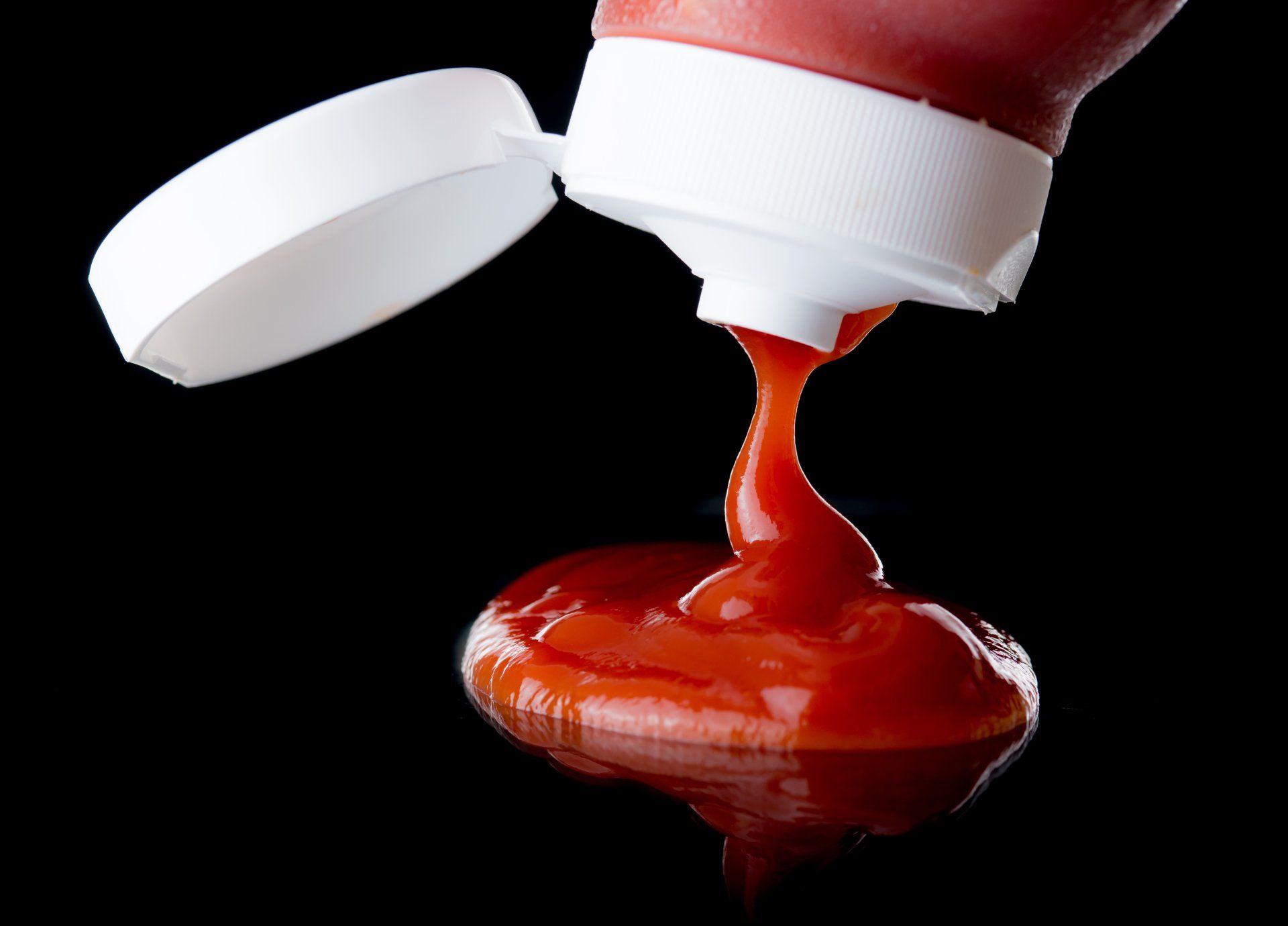 ketchup is being poured from a bottle on a black background