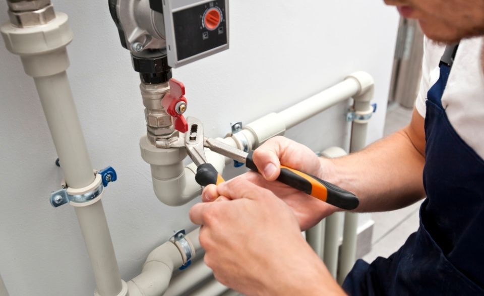 The man is installing the heater system in the house and checking pipes by the wrench