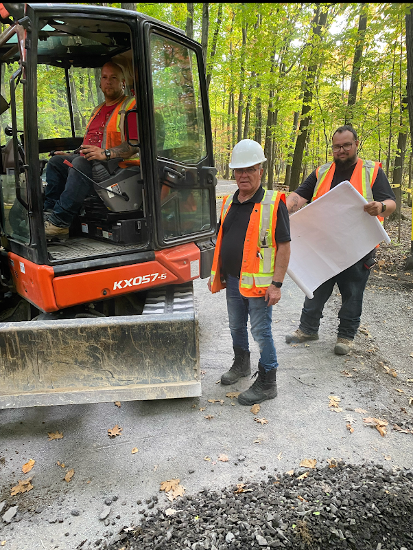 Deux hommes se tiennent à côté d'un bulldozer sur un chemin de terre.