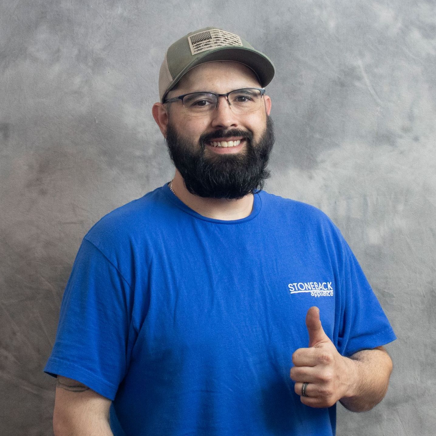 A man with a beard and glasses is wearing a blue shirt and giving a thumbs up