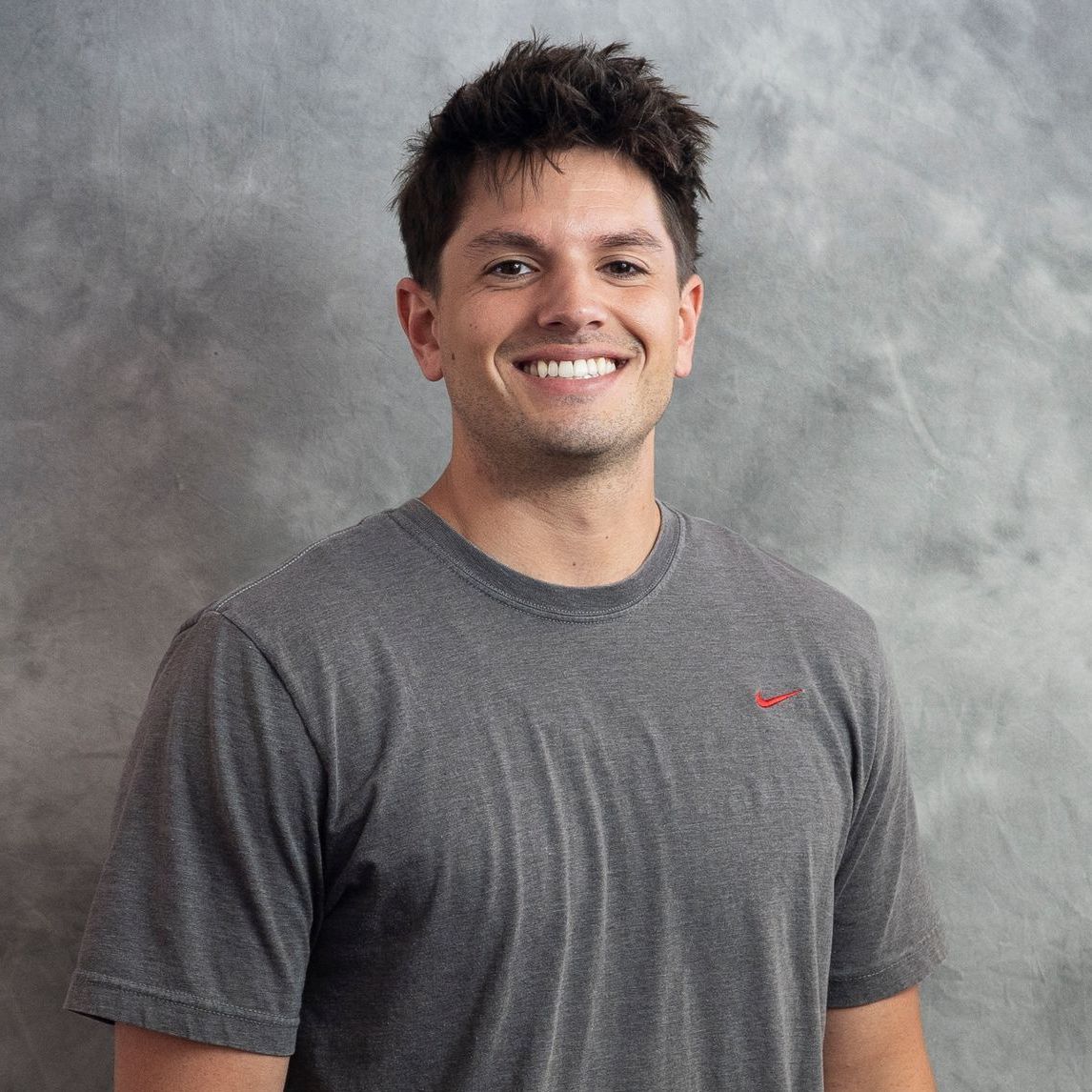 A man wearing a grey t-shirt is smiling for the camera.