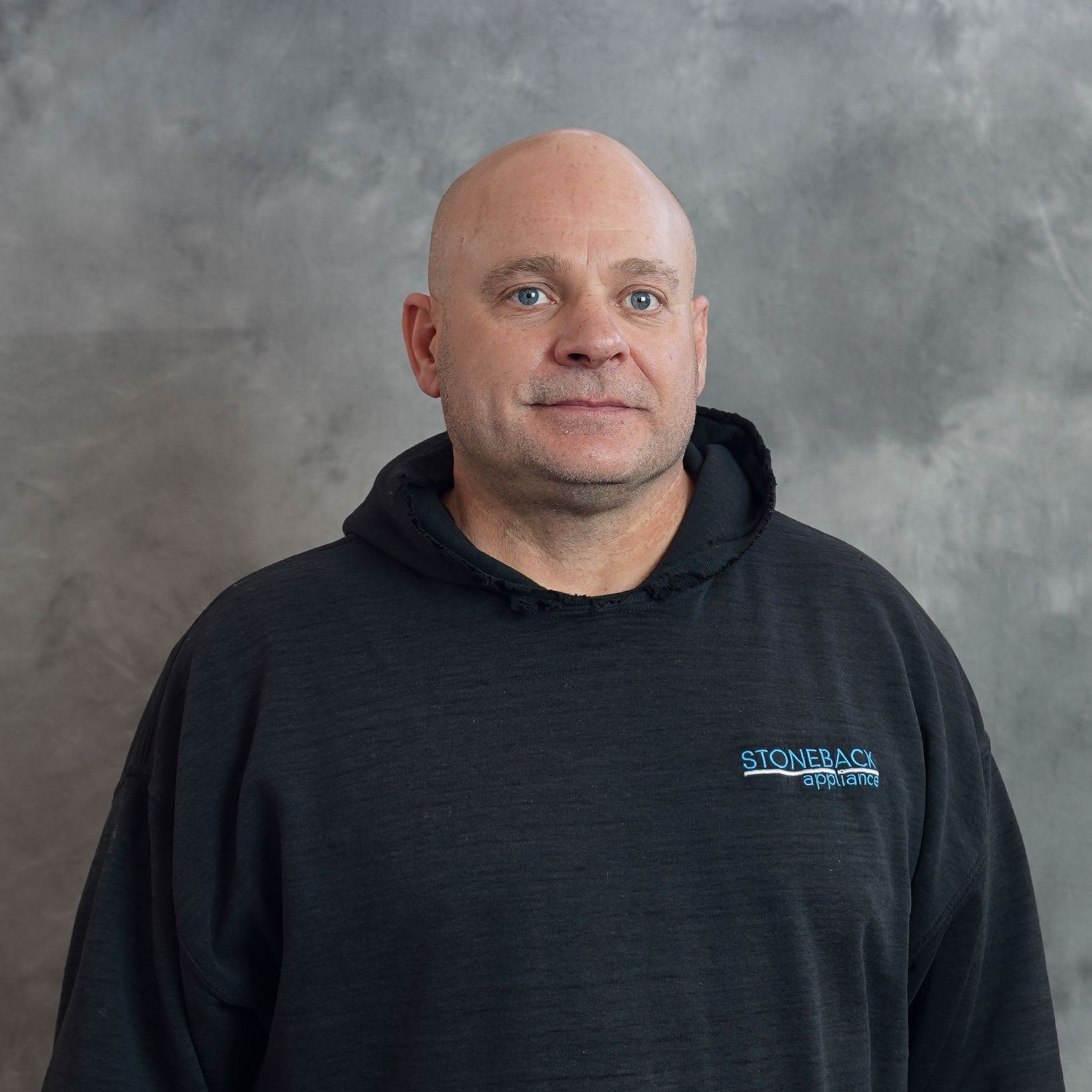 A bald man wearing a black hoodie is smiling for the camera.