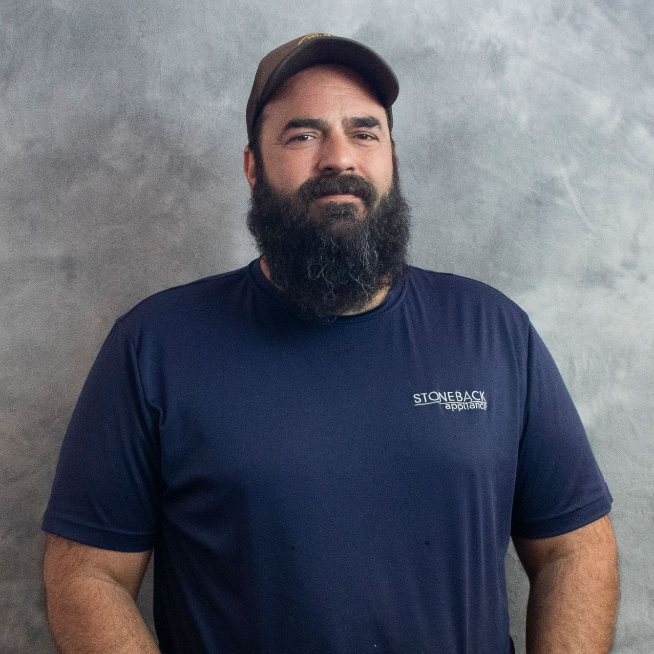 A man with a beard is wearing a blue shirt and a hat.