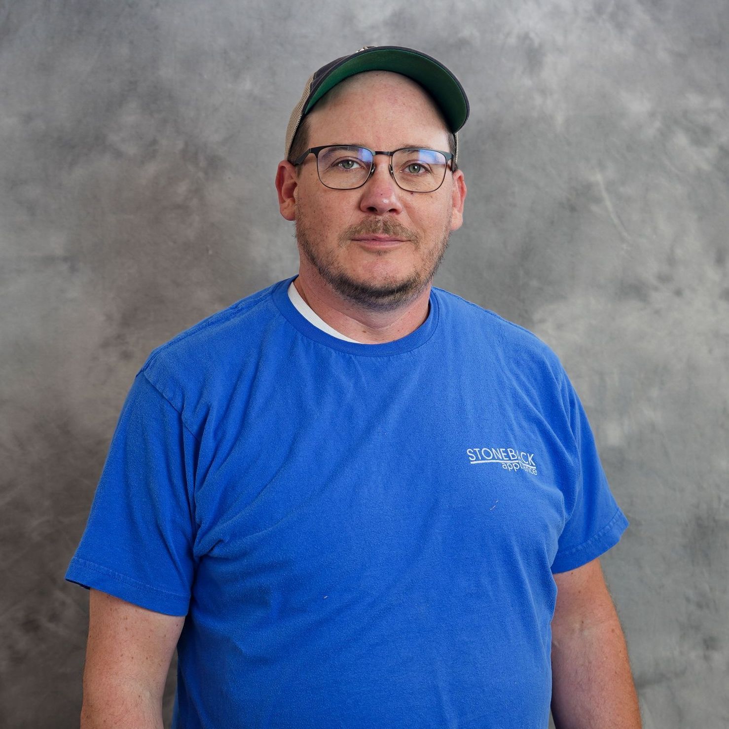 A man wearing glasses and a hat is wearing a blue shirt