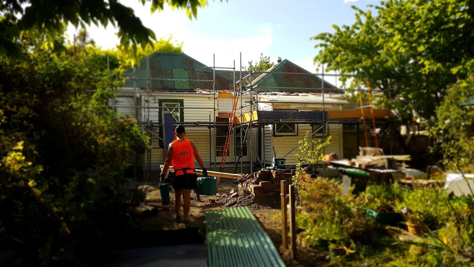 A man in an orange vest is walking towards a house under construction.
