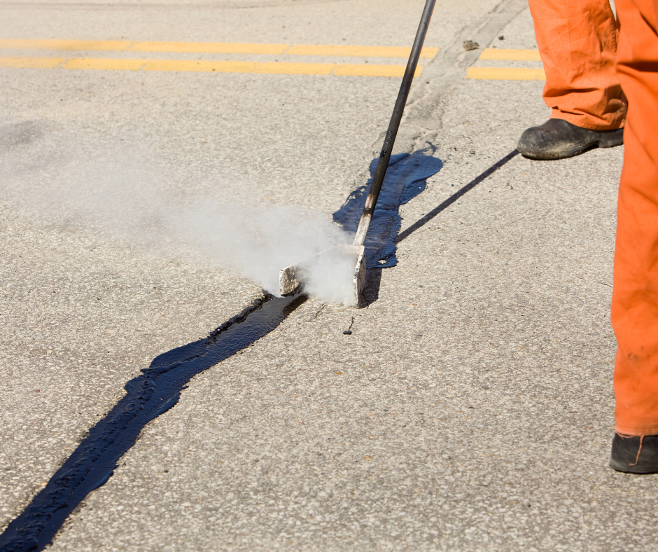 A man in orange pants is spraying asphalt on a road