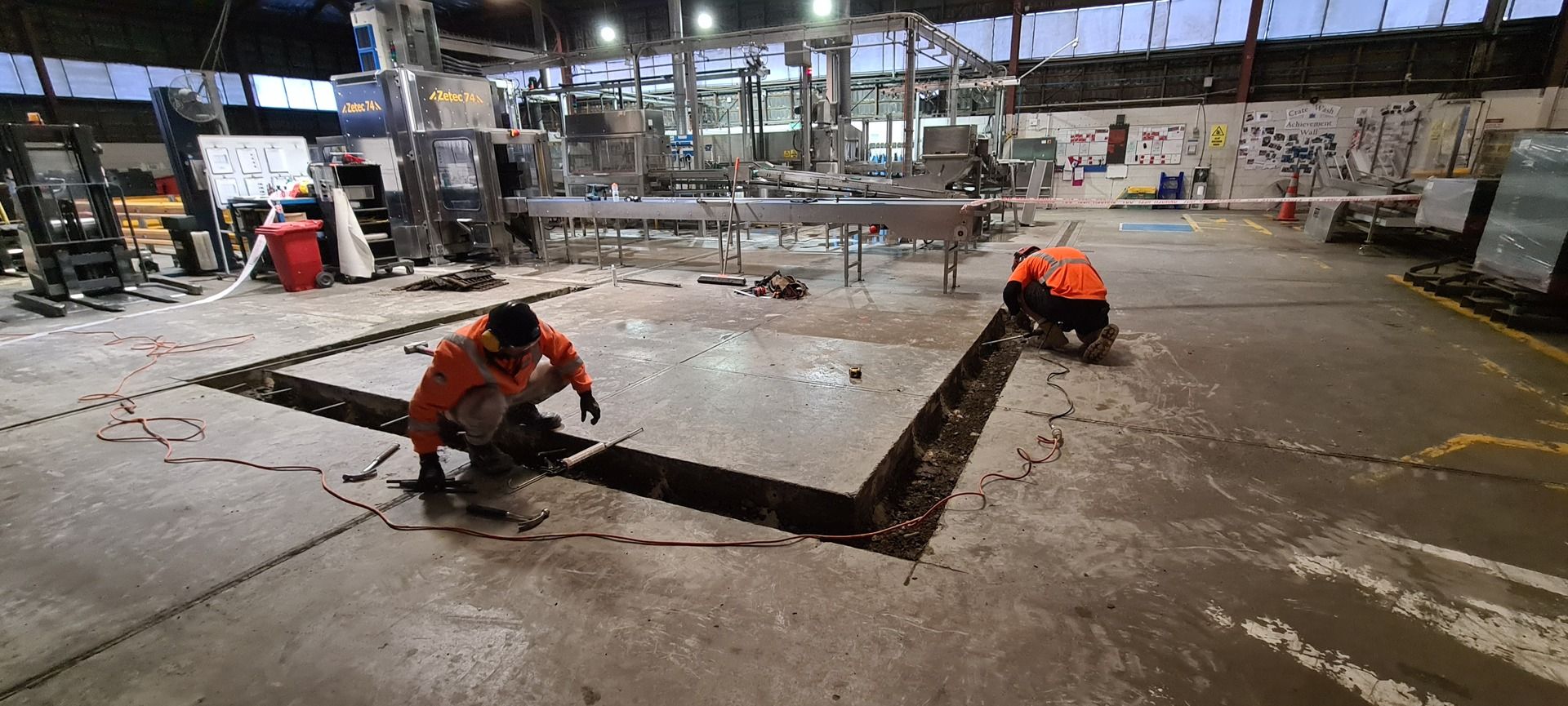 Two men are working on a concrete floor in a factory.