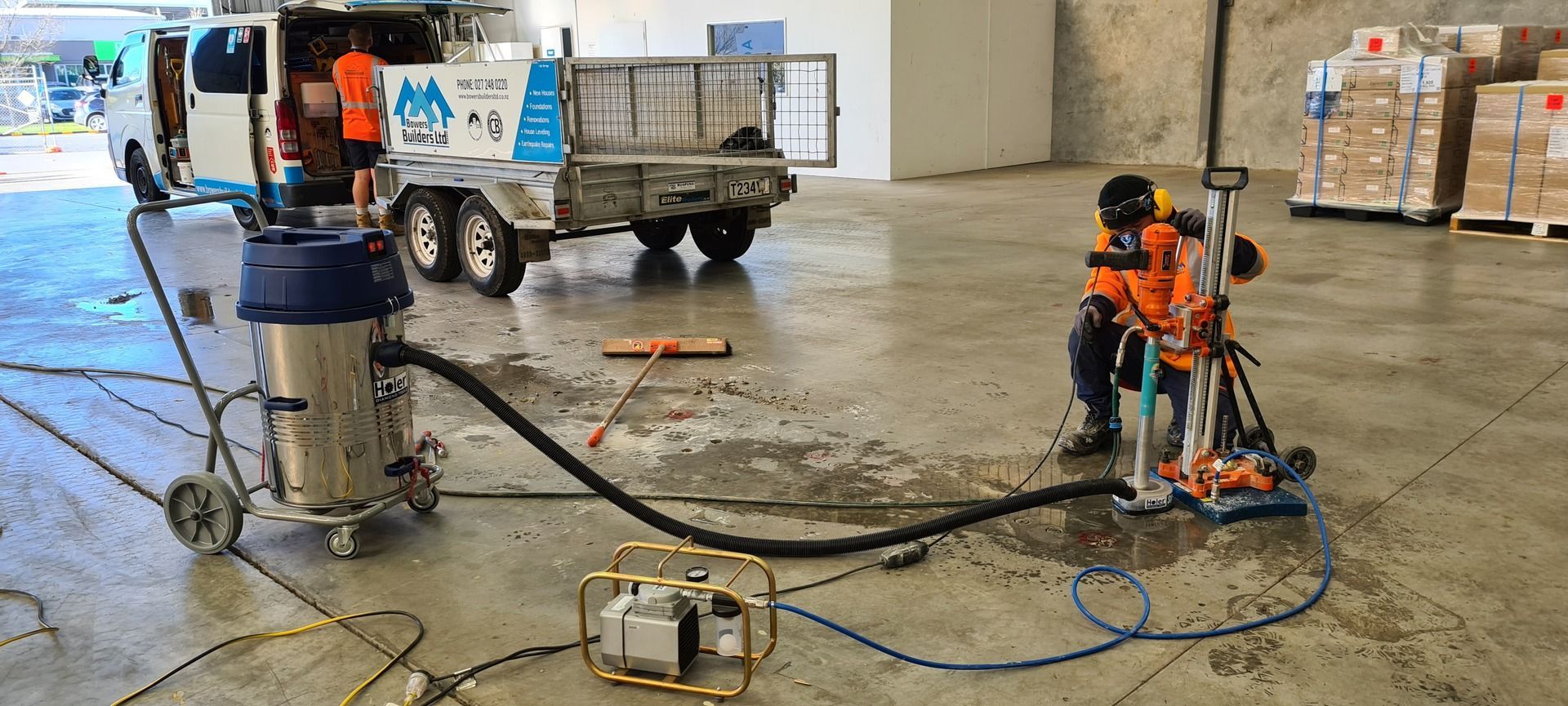 A man is using a vacuum cleaner to clean a concrete floor in a warehouse.