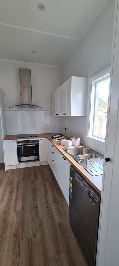 A kitchen with white cabinets , a stove , a sink , and a window.