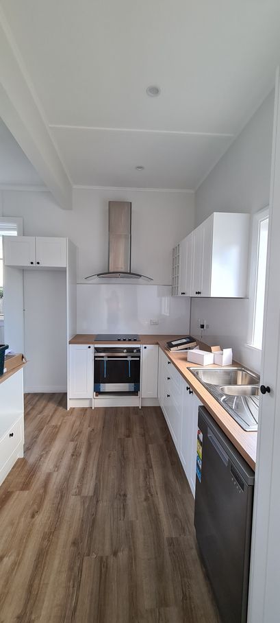 A kitchen with wooden floors , white cabinets , a stove , a sink , and a dishwasher.