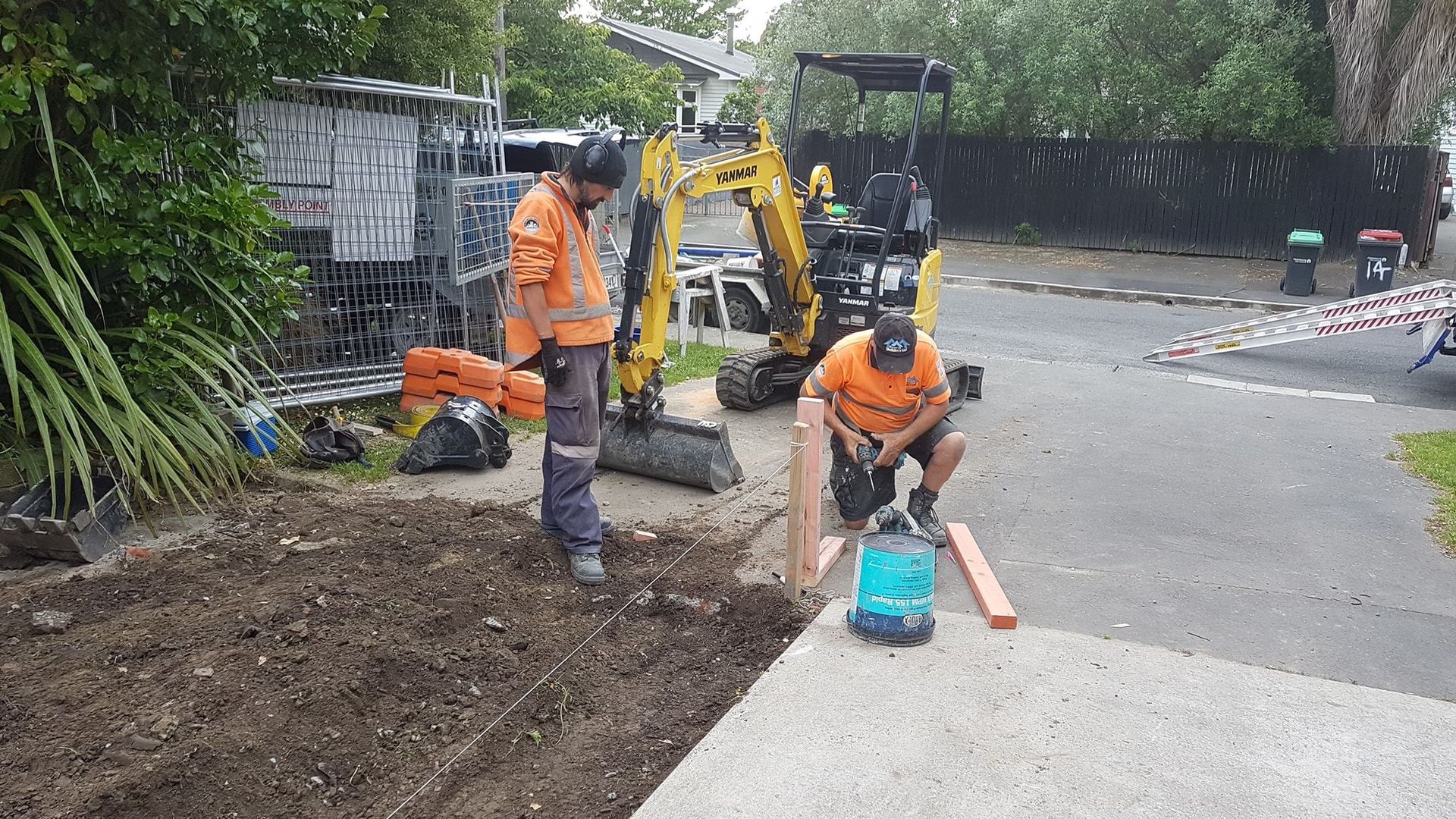 Two men are working on a driveway next to a yellow excavator.