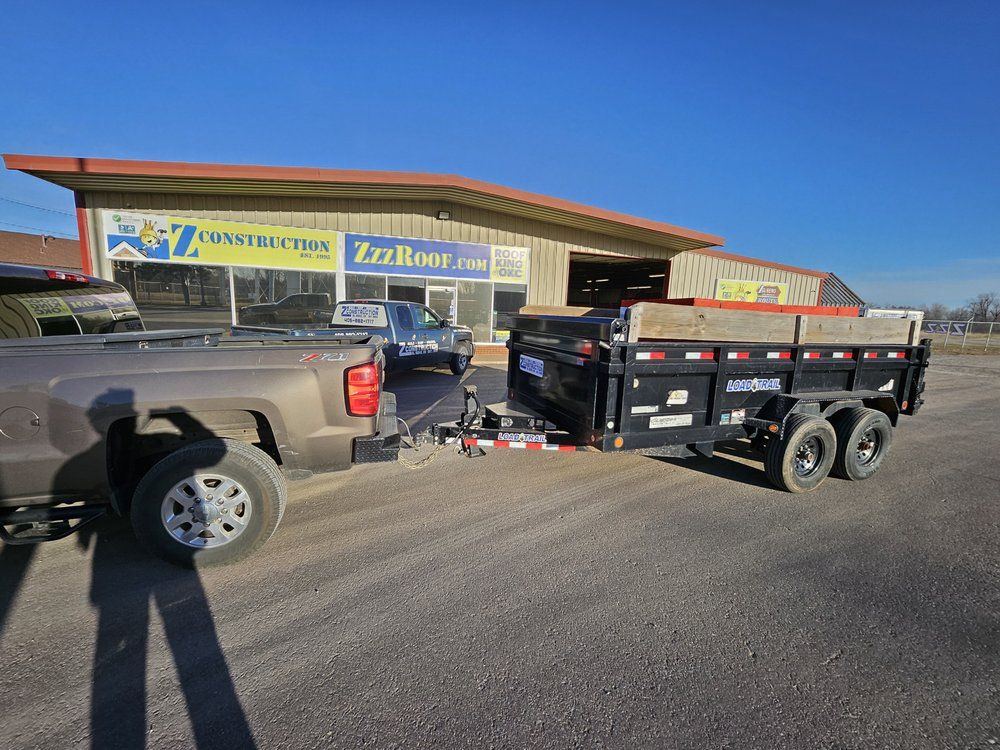 Truck towing a black dump trailer in front of a construction business.