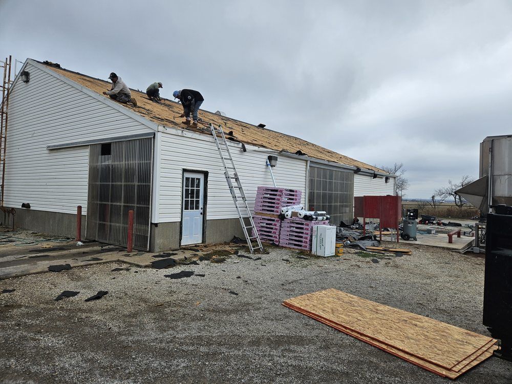 Workers replacing roof shingles on a white building under a cloudy sky. A ladder rests against the roof.