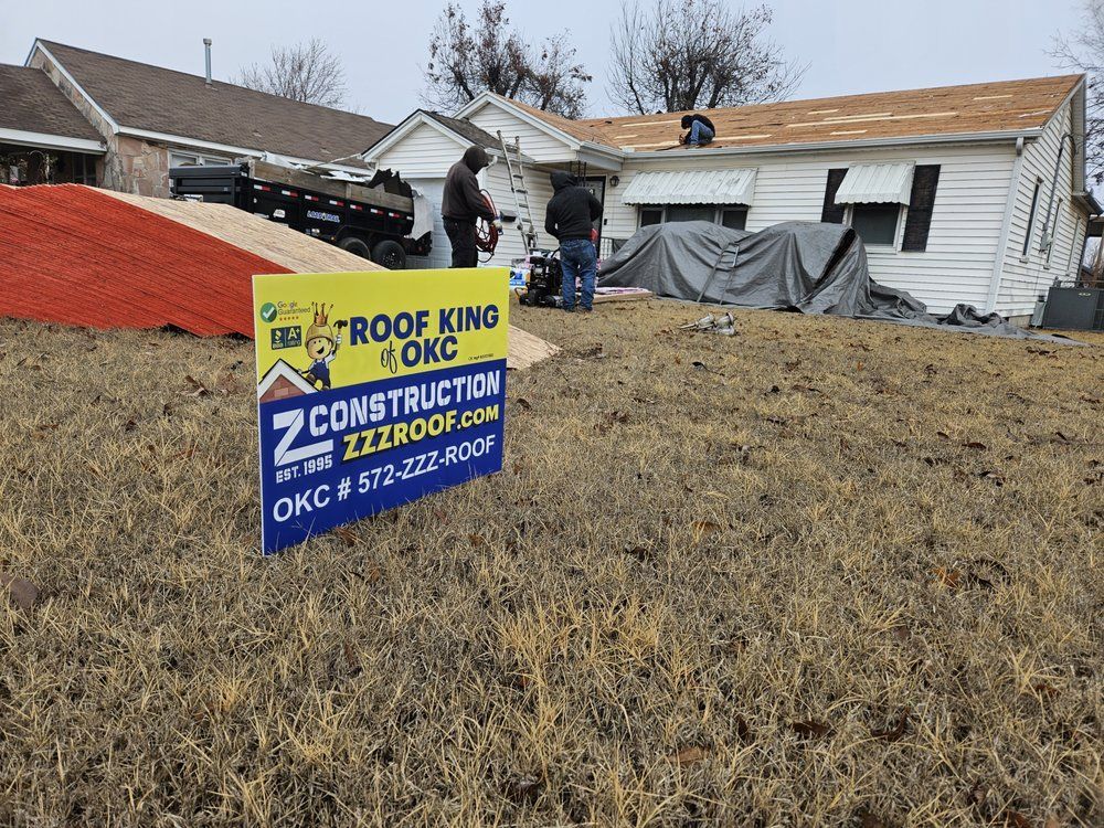 Roofers on a house with a sign for Z2 Construction in OKC. Roofing materials and a trailer are nearby.