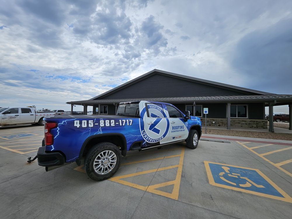 Blue and white truck with company logo parked near building, cloudy sky.
