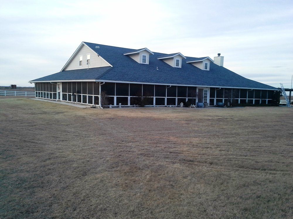 Large house with a wrap-around screened porch, set on a vast, brown, grassy field, under a cloudy sky.