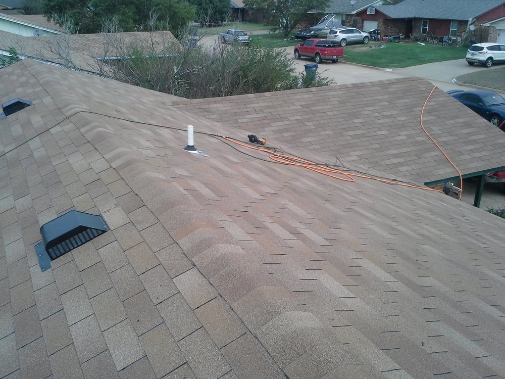 Brown shingled roof with a vent, a cable, and several cars parked in a residential neighborhood.