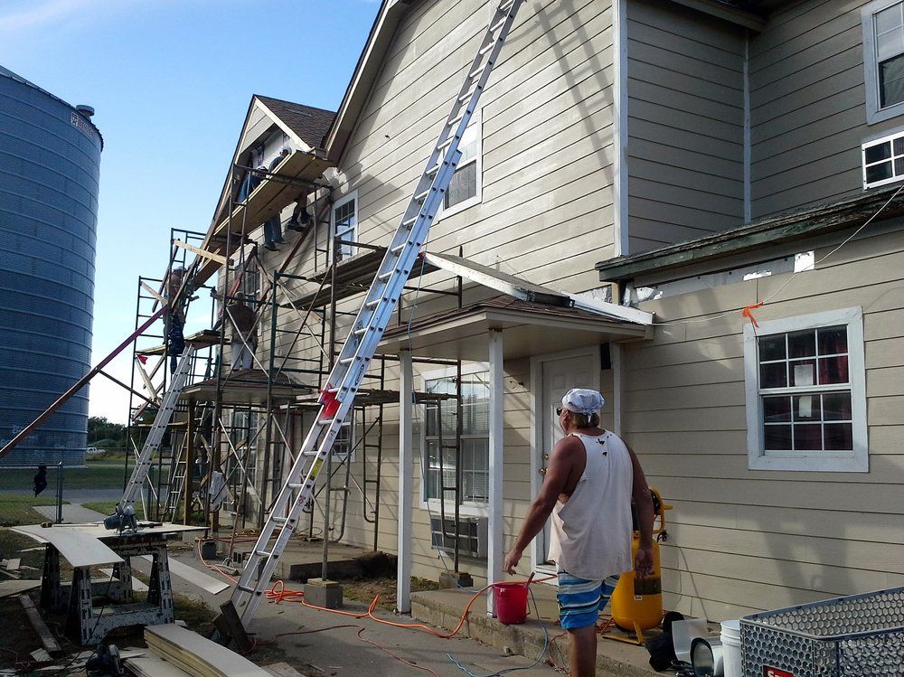 Construction work on the side of a building, with scaffolding and a ladder. Man carries a bucket.