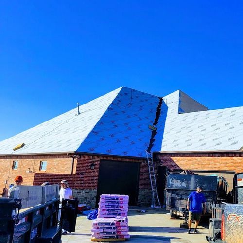 Roofers working on a building with a newly shingled roof under a clear blue sky.