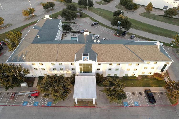 Aerial view of a long, white, two-story building with a light brown roof and a central entrance.