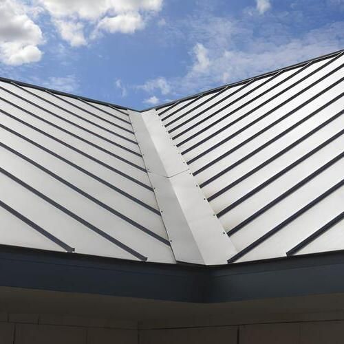 Metal roof with angled panels and ridge cap against a blue sky.