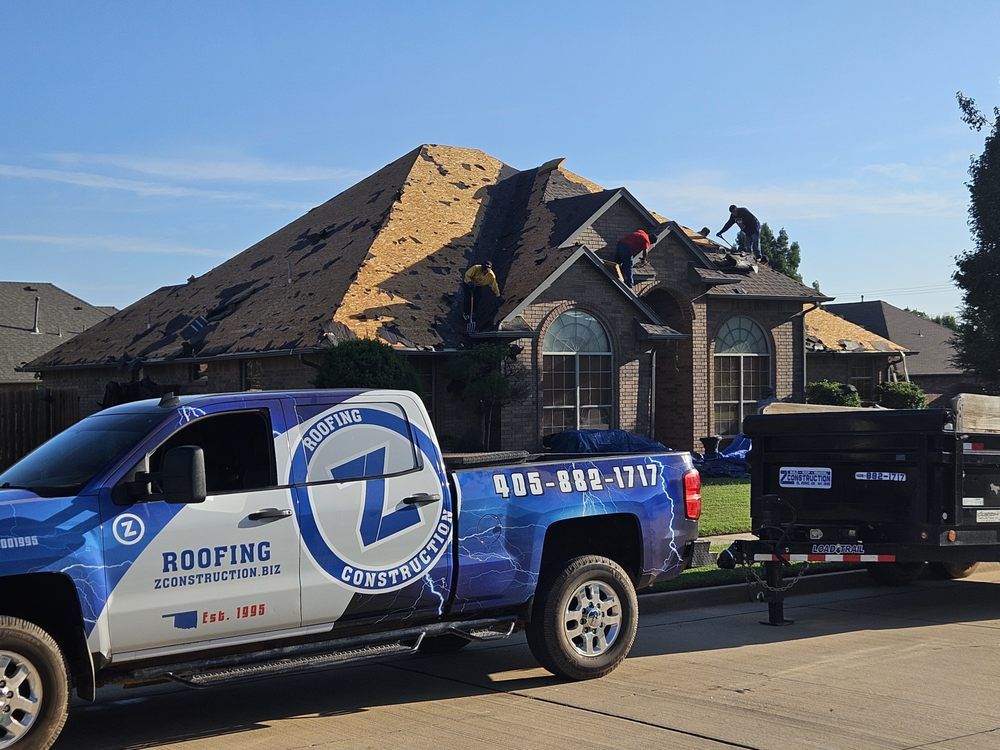 Roofers working on a house with a Z Roofers truck in the foreground.
