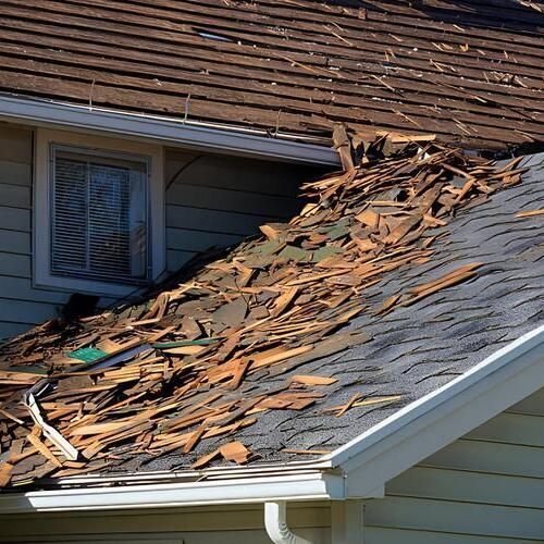 Damaged roof with missing shingles and debris on a residential house near a window and gutter.