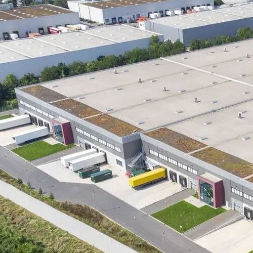 Large industrial warehouse complex with loading docks, trucks, and a green rooftop.
